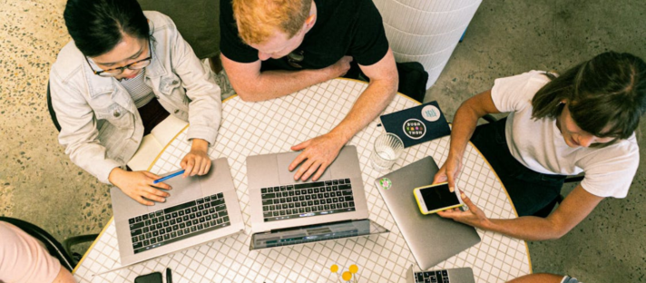 A marketing team discussing effective marketing strategies for plastic surgeons at a table with laptops and smartphones.