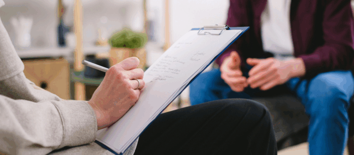A clinic professional taking notes on a clipboard during a patient consultation, highlighting the need for secure, HIPAA-compliant form integration—a must-have among Website Features for Aesthetic Clinics.