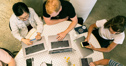 A marketing team discussing effective marketing strategies for plastic surgeons at a table with laptops and smartphones.